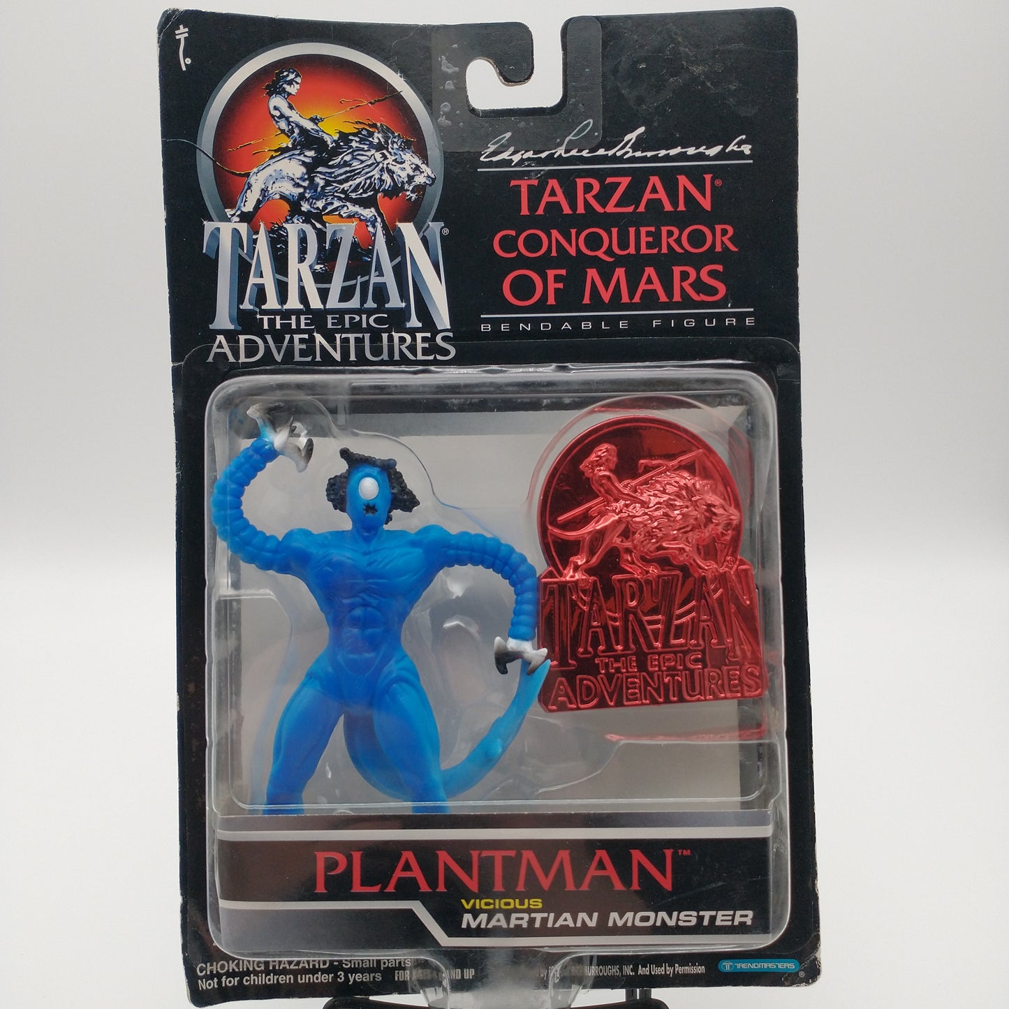 The front of the carton and bubble. Inside the bubble is the action figure planet man, which is blue and has black hair, a single eye, and has clawed hands and a tail. There is a red chrome medallion to the right of the figure.