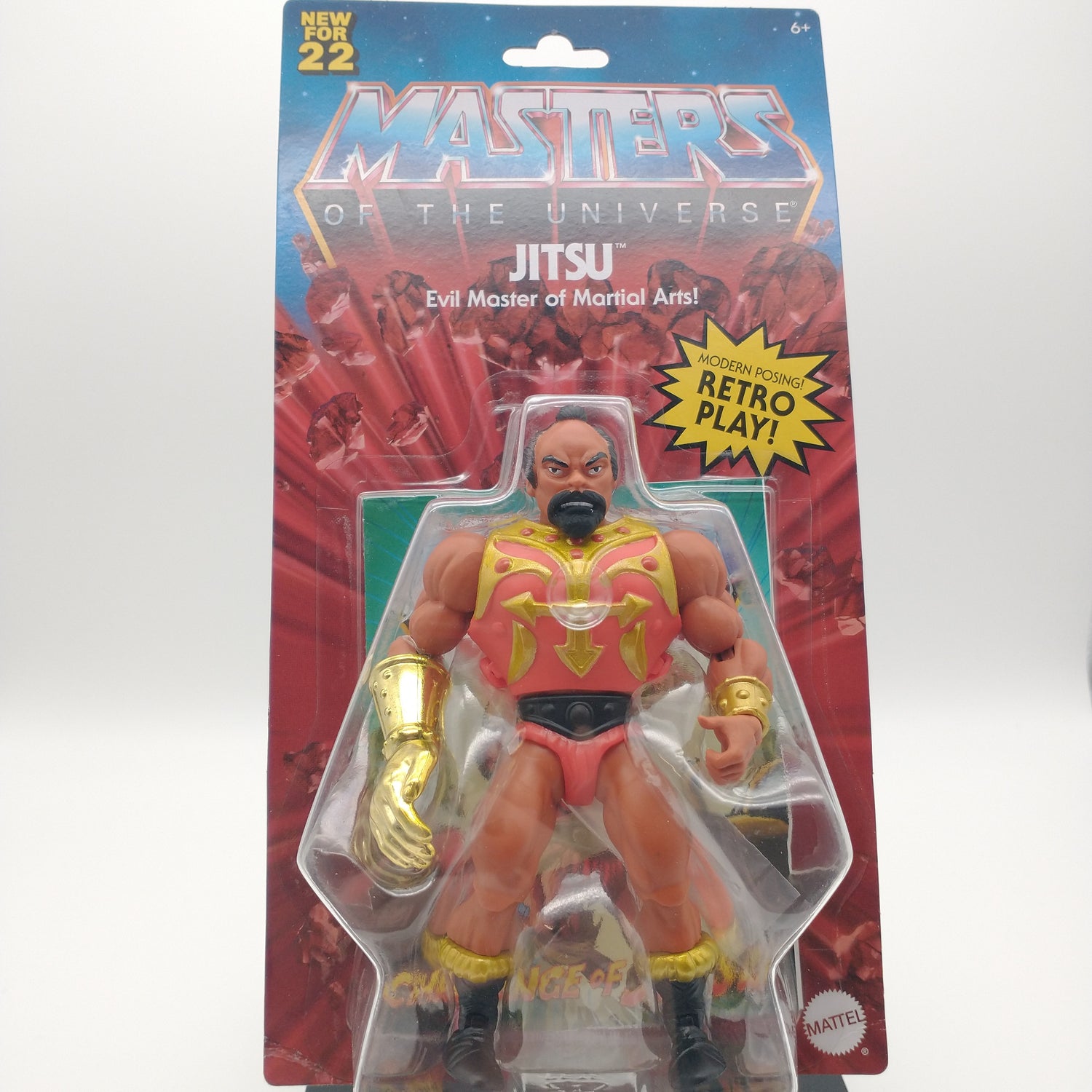 The front of the box and bubble. The bubble is sealed, the action figure inside has a dark complexion and is wearing a red leotard with gold detailling. His left hand is golden.