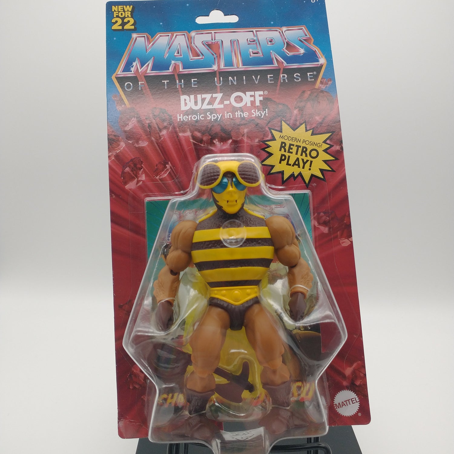 The front of the box and bubble. The bubble is sealed, the action figure inside is a humanoid with tand arms and legs wearing a black and yellow striped leotard, a yellow mask with green eyes, and a helmet with two brown spots.