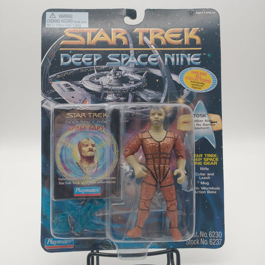 The front of the box and bubble. The bubble is sealed, the action figure inside is a lizard scaled humanoid wearing an orange jumpsuit