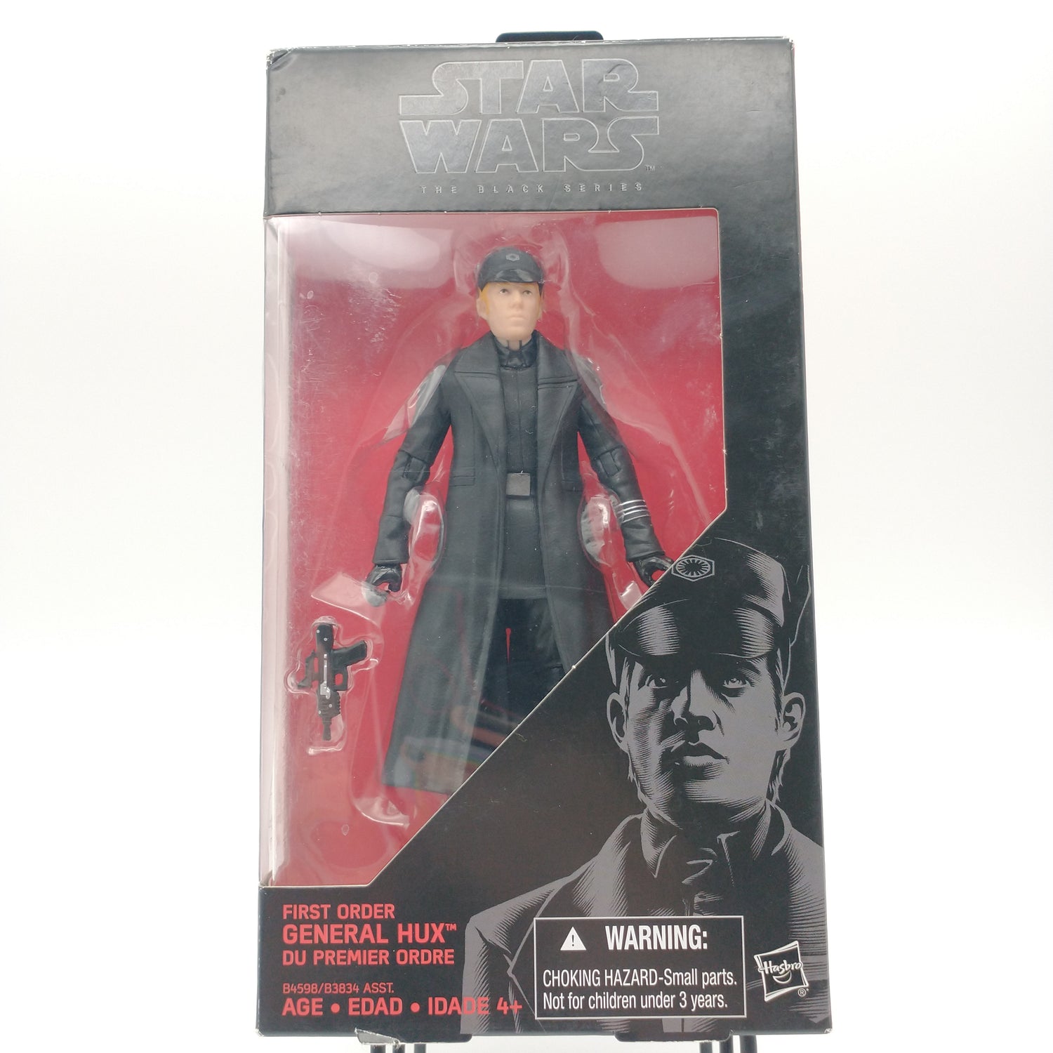 The front of the box and bubble are intact. The action figure is standing against a red background. He is wearing a military uniform with a black trenchcoat and a black hat. Next to him is a small black gun.