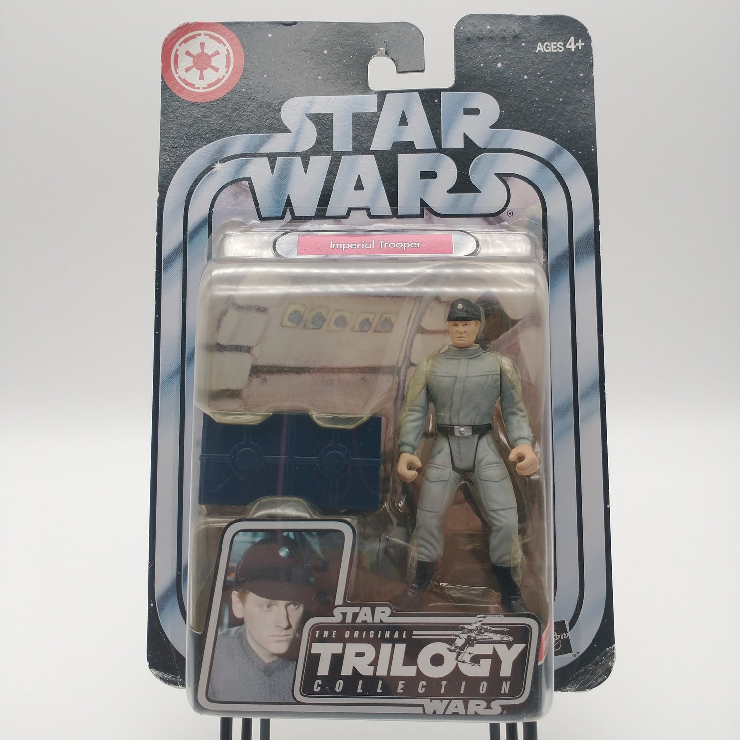 The front of the box and bubble. The bubble is sealed but slightly yellowed. The action figure is inside, he is a man wearing a gray suit and a black hat. 