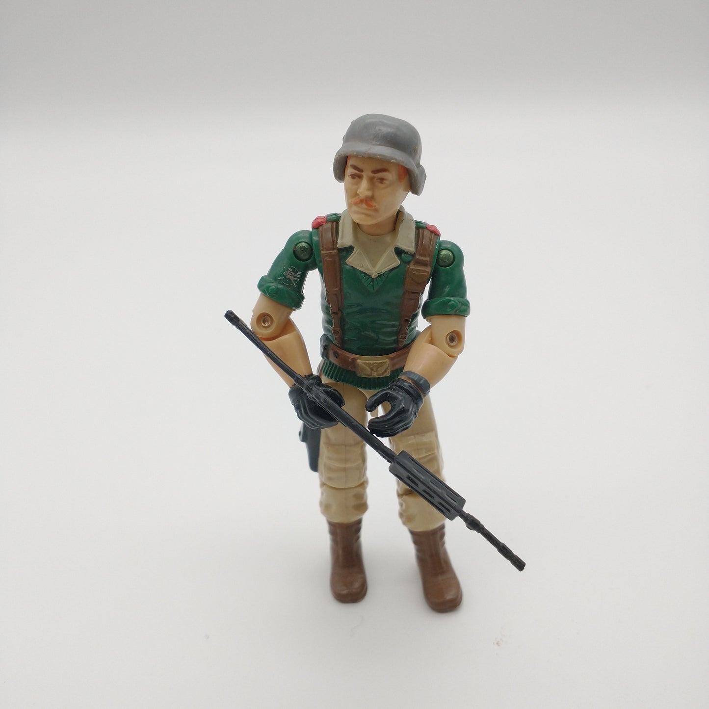 The figure is holding a long thin gun, wearing a silver hat and green shirt with suspenders and tan pants